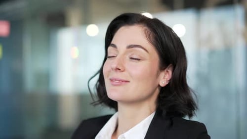 Businesswoman in formal attire taking a moment to relax with closed eyes in an office environment.