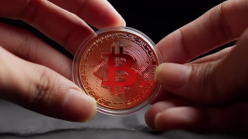 Hands Holding Bitcoin Crypto Currency in Plastic Coin Case Against Dark Background, Close Up