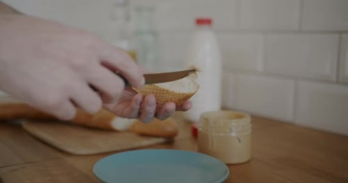 Spreading Peanut Butter on Fresh Baguette in Kitchen