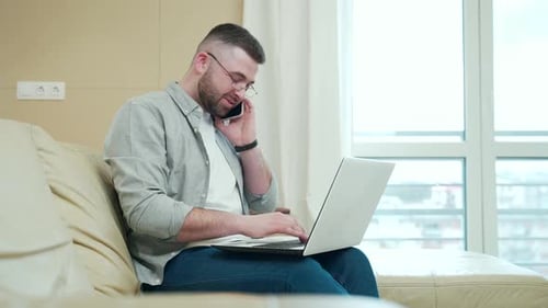 Man Working on Laptop and Talking on Phone