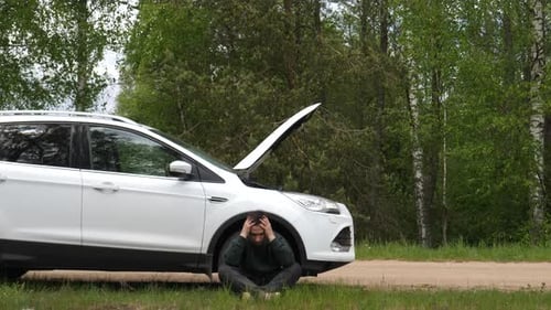 Verärgerter Mann sitzt am Straßenrand in der Nähe einer kaputten Autonothaltestelle