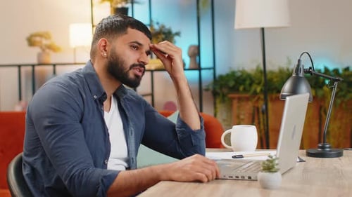 Overtired Stressed Tired Indian Man Freelancer Bored with Laptop While Sitting at Home Office