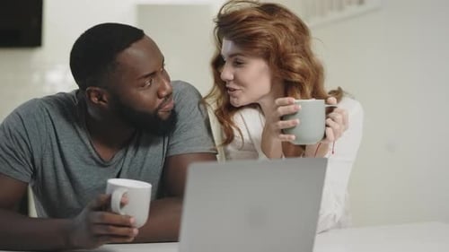 Couple laughs, watches laptop, and drinks coffee
