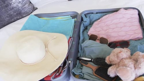 A suitcase is open, revealing neatly packed clothes and a teddy bear
