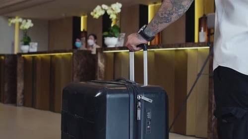 Man with Tattooed Arm with Suitcase Walking in Hotel Hall towards Reception