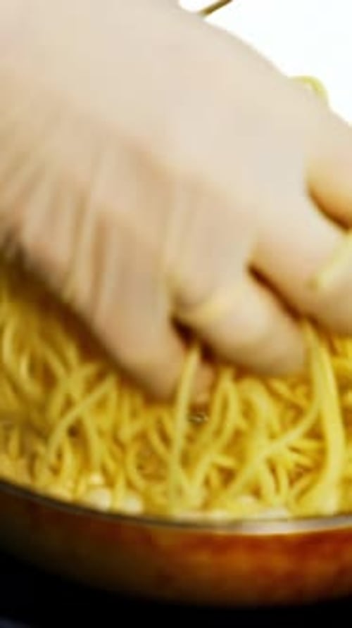 Hand Adding Cooked Spaghetti to Cream Sauce in Pan