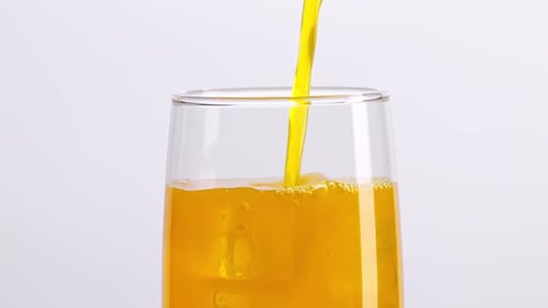 Close Up Of Orange Juice Being Poured Into A Glass With Ice Cubes On White Background