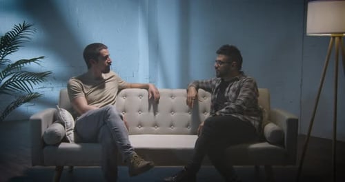 Men Talking on Couch in Dimly Lit Living Room