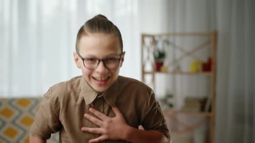 Un écolier de premier cycle éclate de rire en se tenant la main contre la poitrine Un écolier joyeux à lunettes éclate
