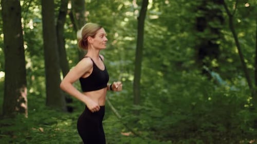 Woman Jogging in Green Forest During Daytime for Fitness and Healthy Living