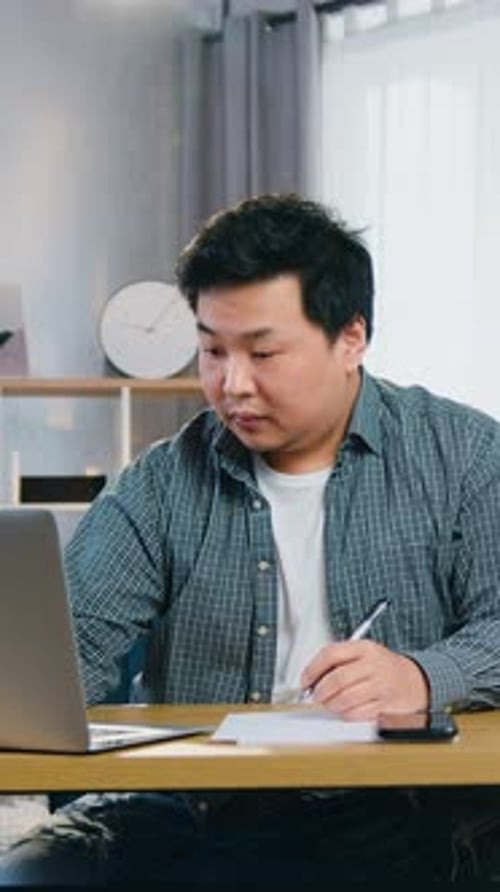 Man Uses Laptop and Takes Notes at Desk