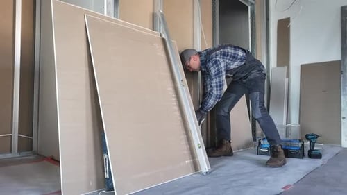 Construction Worker Measuring Drywall with Level Indoors