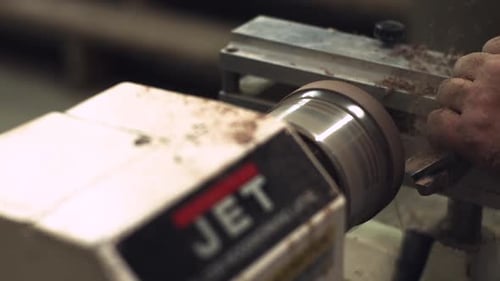 3/4 Slider shot of a carpenter carving wood at a factory lathe with saw dust