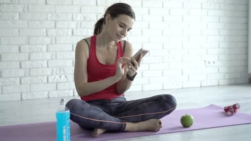 Young Woman Using Phone After Workout on Yoga Mat