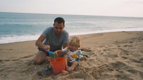 Closeup of a Child and His Father Playing with a Shovel and Bucket on the Sand at the Beach
