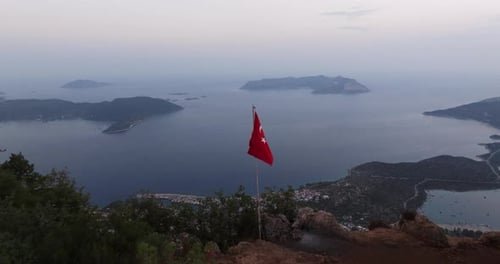 Turkish flag on a hilltop overlooking Kas at dusk, with a serene coastal backdrop of town along idyl