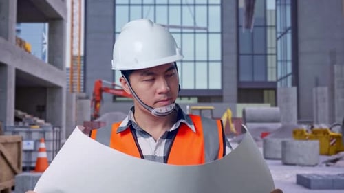 Nahaufnahme eines asiatischen männlichen Ingenieurs, der auf der Baustelle den Bauplan in seinen Händen betrachtet
