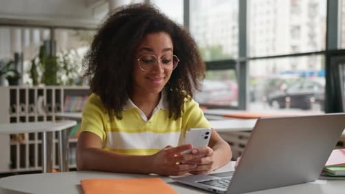 African American Happy Smiling Girl Student Chatting Typing Mobile Phone at Table in University