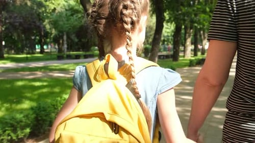 Mom Leads the Hand of Little Girl an Elementary School Student Back to School