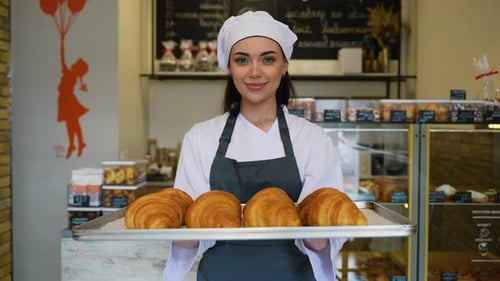 Young Woman Baker Holds Croissants in Bakery