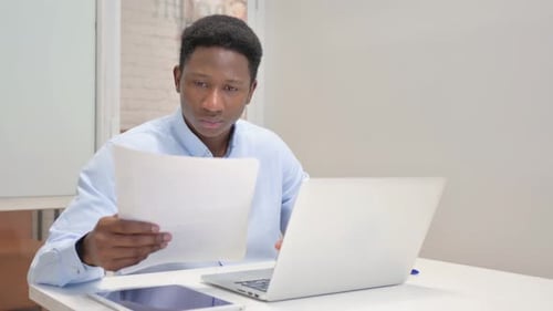 Man Reviews Documents While Using Laptop
