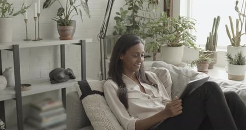 Woman Relaxes on Sofa Using Tablet at Home
