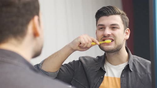 Close-up of young charismatic man brushing his teeth.