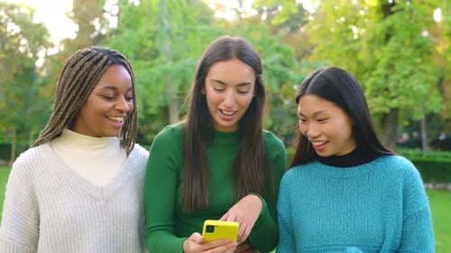 Multiethnic Friends Smiling While Using the Mobile in a Park