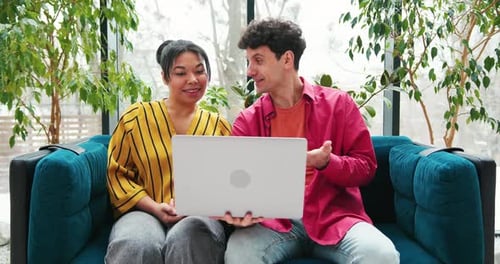 Smiling Colleagues Sitting on Comfortable Sofa in Modern Office Having Video Call Waving Hand