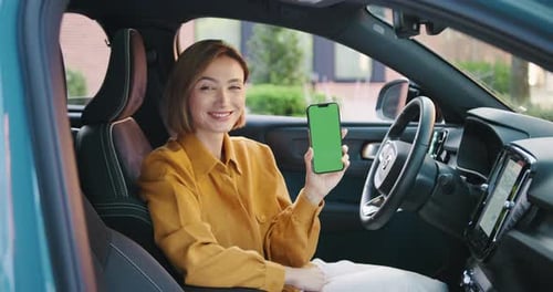 Confident Young Businesswoman in Casual Attire Sitting in a Car Smiling and Holding a Smartphone