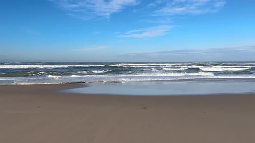 Sea waves and surf crashing in over sandy beach in winter Portugal.