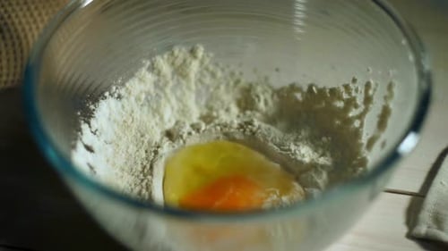 Broken Fresh Chicken Egg Falls Into Glass Bowl with Flour. Close Up