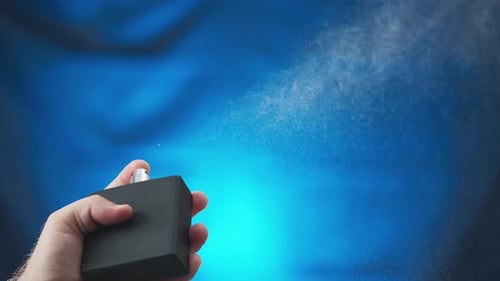 Hand Sprays Perfume from Black Bottle on Blue