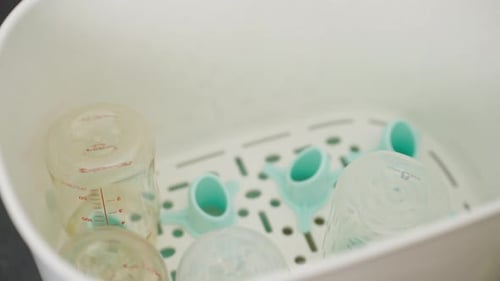 hand of mother feeding baby milk bottle into the Steam sterilizer
