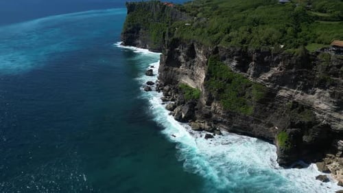 Ocean waves moving toward the cliffs on the coast of Uluwatu in Bali, Indonesia. Aerial.