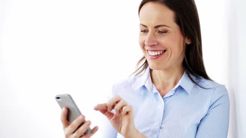 Smiling Woman Typing on Smartphone in Bright Room