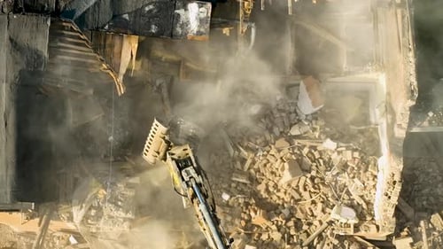 High-angle view of an excavator tearing down a building, surrounded by dust and debris during a demo