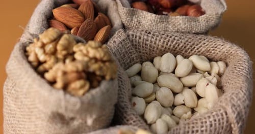 Different types of nuts in bags on brown background, spinning. Closeup view
