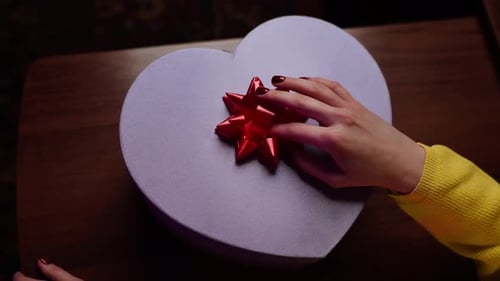 Woman Places a Bow on Heart-Shaped Gift
