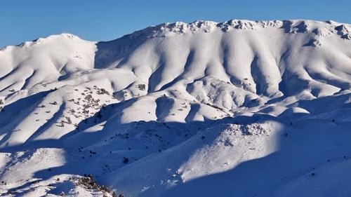 Aerial View of Snowy Mountain Landscape and Forest Under Winter Sunlight