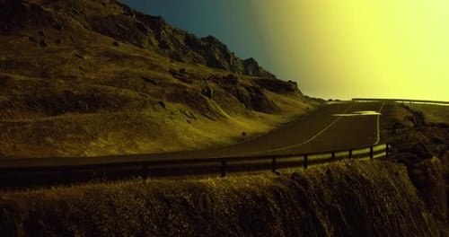 Curving Mountain Road Under Bright Sun Setting Near Rocky Landscape