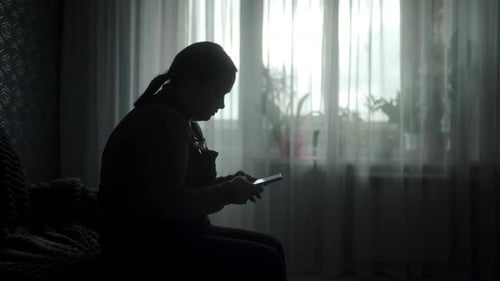 Woman Using Phone Device in Darkened Room