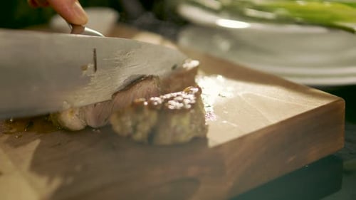 Close-up of Prepared Piece of Meat Being Cut with use of Knife and Fork on a Cutting Board. In Back
