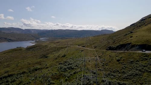 Drone Flying Over High Voltage Power Line And Green Mountain Hills With Lake In The Distance on West