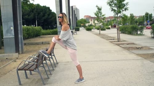 Young sportswoman in city stretching leg on bench in super slow motion
