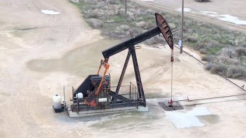 An oil pumpjack in motion in a desolate field, overcast day, industrial scenery, aerial view
