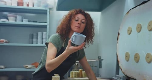 Woman Inspecting Pottery Mug in Studio