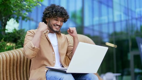 Young Adult Man Celebrates with Laptop on Bench