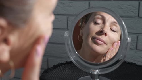 Woman Applies Cream to Face in Mirror