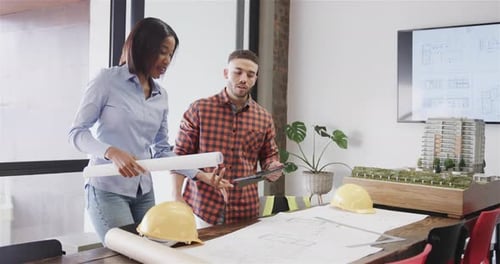 Diverse male and female architects with tablet discussing blueprints standing in office, slow motion
